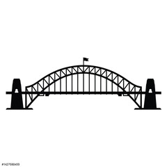 Silhouette of a large steel arch bridge with a flag on top