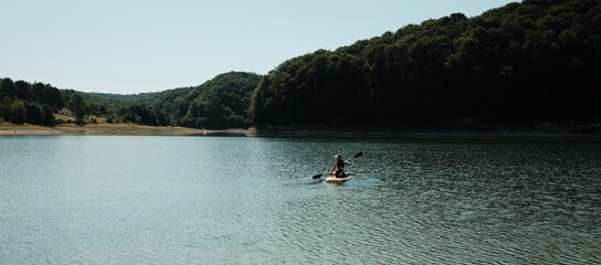 Young woman paddleboarding with a Australian shepherd dog on a calm lake surrounded by forested...