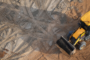 Yellow JCB excavator working at a construction site, top view with detailed tire tracks in the sand  © belavinstock