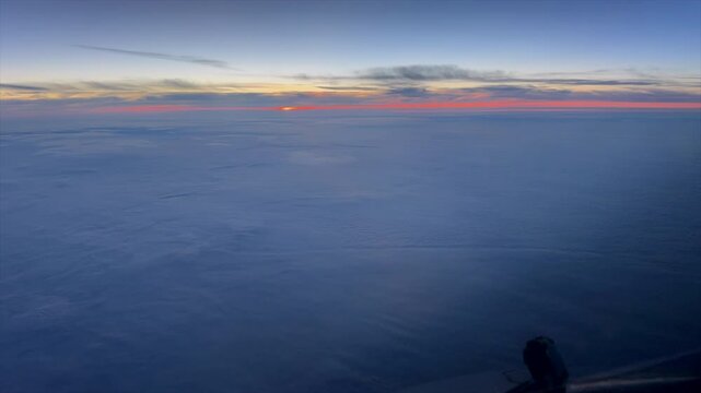 Time-lapse captured from the cockpit of a commercial airliner as the sun rises over the horizon at cruise altitude. The deep blue atmosphere gradually transitions to warm morning light, offering a dra