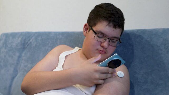 teenager man with diabetes checking blood glucose level at home using continuous glucose monitor. The boy checks the glucose level