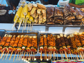 Thai street food stall with grilled meat and corn on skewers. Concept of culture, tradition, nutrition, flavor, community and culinary lifestyle.