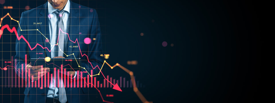 Businessman using tablet with falling stock market chart and red arrow indicating financial crisis and global economic downturn on dark background.