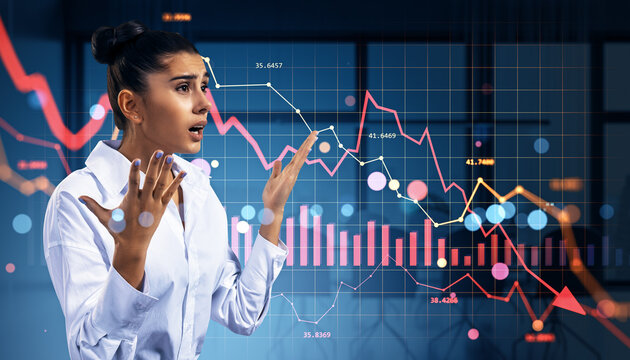 Worried businesswoman reacting to sharp financial market crash with red declining stock graphs over modern office background hologram chart display.