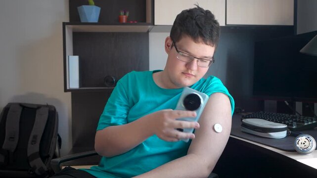 teenager man with diabetes checking blood glucose level at home using continuous glucose monitor. The boy checks the glucose level