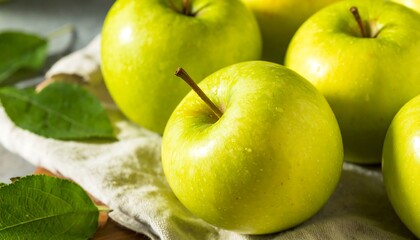 Fresh, vibrant green apples are displayed beautifully on a light-colored cloth, with fresh leaves adding a touch of natural elegance.