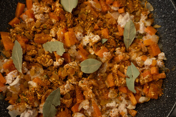 A close-up shot of cooked chicken, carrots, and onions mixed with spices, raisins, and bay leaves in a pan. This image captures the rich, colorful, and aromatic mixture that forms the base of Plov. Id