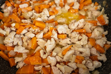 A close-up shot of chopped chicken, diced carrots, and onions cooking together in a frying pan. The ingredients are browning and glistening with oil. This image illustrates a key step in making Plov