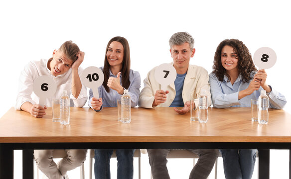 Panel of judges voting with score signs at table on white background