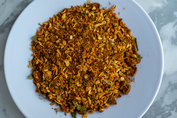 A pile of golden-brown spices, a key ingredient for Plov, is presented on a small white plate against a marble background. The mix of textures and vibrant colors adds visual interest. Perfect for food