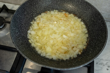 A close-up shot of chopped white onions sizzling in hot oil within a dark frying pan. The onions are beginning to soften and turn translucent. This image is perfect for illustrating an early cooking s