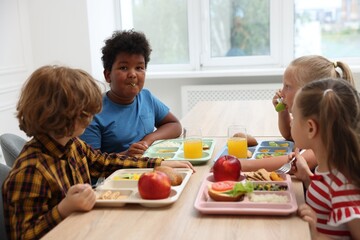 Little kids eating lunch at wooden table in school canteen