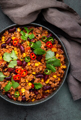 Mexican meet Chili with beef, beans, paprika, corn, cilantro, jalapeno in tomato sauce, in frying pan, rusty green background top view