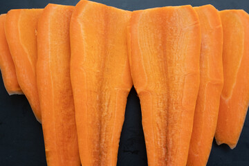 A low-angle, close-up shot of freshly sliced carrots arranged on a dark, textured surface. The...