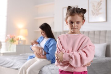 Jealous little girl upset about mom spending time with newborn baby at home, selective focus