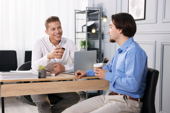 Coworkers with coffee discussing project together at desk in office