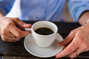 A person’s hands gently hold a white coffee cup on a dark table. The close-up view captures a simple and peaceful moment of relaxation