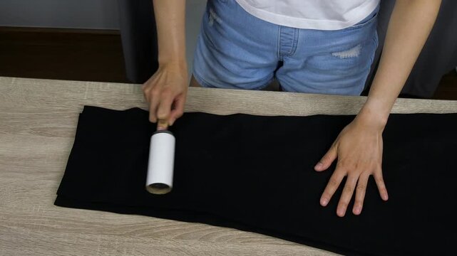 Close-up of person using lint roller to clean black pants, clothing care and cleaning concept