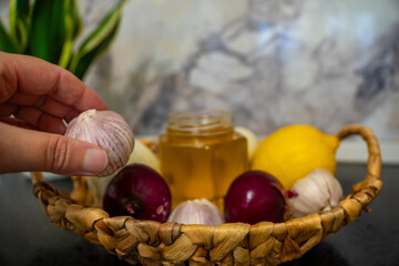 Still life with a jar of honey, red and white onions, garlic and lemon, and a flower in the background on a dark background