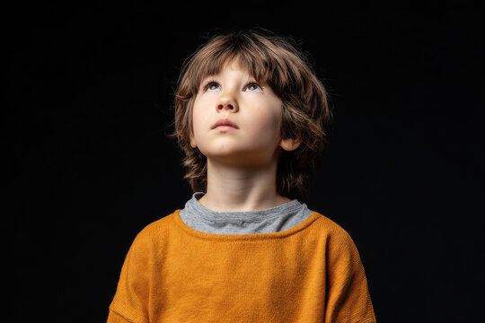 young boy gazes upwards with despair in his eyes against clean solid color background