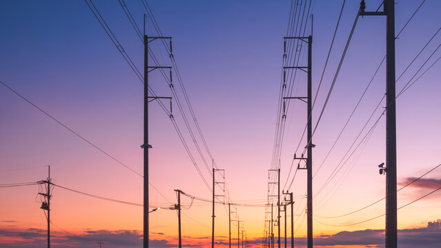 Silhouette row of electric poles with cable lines on street in industry settlement area against colorful evening sky background, low angle and front view with copy space