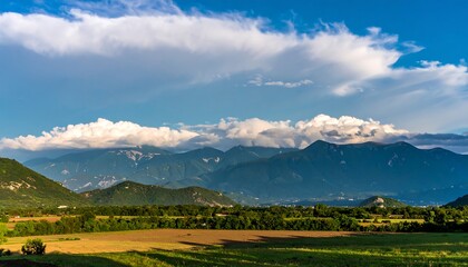 Obraz premium Panoramic view of a valley with rolling hills and mountains under a vibrant blue sky dotted with fluffy white clouds.