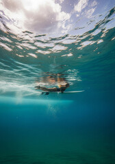 Obraz premium Underwater Surfboard: The surfboard floats effortlessly just beneath the surface of the ocean, beneath a partly cloudy sky, showcasing the serene beauty of surfing. 