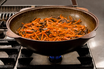 Traditional Uzbek dish being prepared in a large pot with vibrant carrots and tender meat, pilaf, showcasing rich culinary heritage and cooking techniques. Copy space, menu