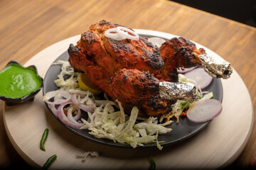Crispy delicious whole chicken tandoori with vegetables or salad served in plate 