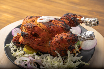 Crispy delicious whole chicken tandoori with vegetables or salad served in plate 