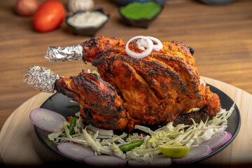 Crispy delicious whole chicken tandoori with vegetables or salad served in plate 