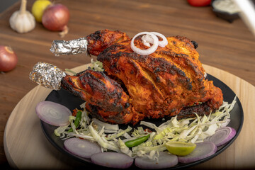 Crispy delicious whole chicken tandoori with vegetables or salad served in plate 