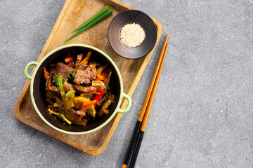 Beef stir fry in a frying bowl top view, Asian meat with vegetables on a grey background with copy space for text