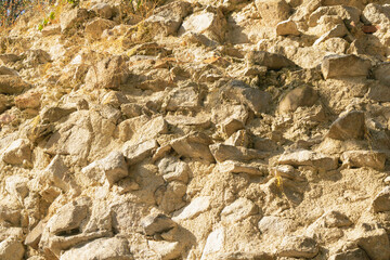 Rough stone wall with dry grass and uneven rocky surface in warm sunlight
