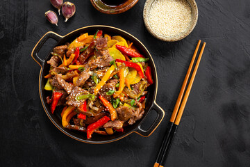 Beef stir fry in a black frying pan top view, Asian meat with vegetables on a black background top view