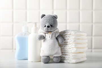 Many different baby accessories and toy bear on table near tiled wall