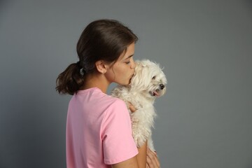 Happy teenage girl with Maltese dog on grey background