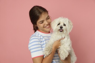 Happy teenage girl with Maltese dog on pink background