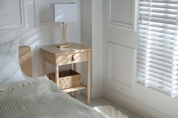 Bedside table with lamp near bed indoors