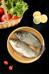 Fresh Raw Carp Fish with Vegetables and Lemon Slices in Wooden Bowl on Dark Background