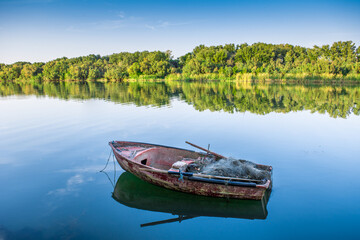 Obraz premium A red boat on river with a beautiful calming reflection of both boat itself and the surrounding Forest trees. , Scenic River Cruise on a Traditional small wooden Fishing with Ropes and Calm Views.