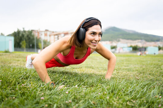 A woman between 40 and 50 years old is training outdoors in sportswear.The woman is doing push-ups on the lawn.Concept of middle-aged women doing sports.
