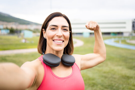 A woman between 40 and 50 years old is training outdoors in sportswear.The woman takes a selfie showing her biceps to the camera.Concept of middle-aged women doing sports.