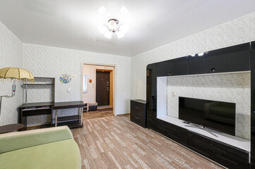 cozy living room with a TV, a couch, and a desk. The walls are wallpapered, and the floor is wooden