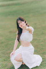 Fototapeta premium Embrace the Moment: A woman, radiant and joyful, playfully gestures towards the camera against the verdant backdrop of a lush meadow, embodying pure happiness.