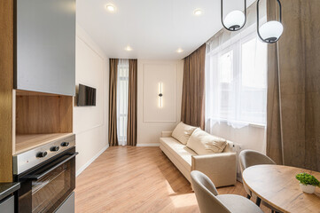 Cozy living room with a beige sofa, wooden floor, curtains, a round table, and a TV on the wall