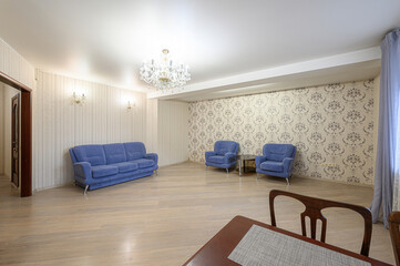 bright living room featuring a blue sofa and armchairs, patterned wallpaper, a chandelier, and light wooden floors