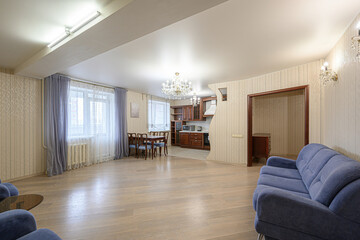 spacious living room featuring a blue sofa, dining set, and kitchen view, all under a bright ceiling with chandeliers