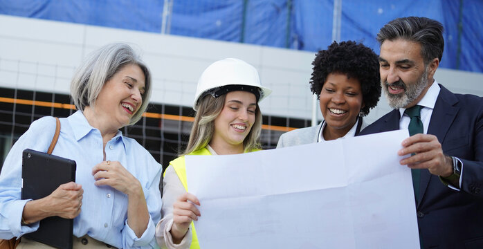 Diverse team of architects and engineers reviewing blueprints outside a building under construction, expressing joy and collaboration
