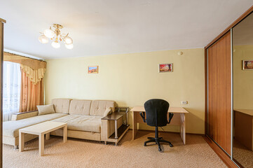 Cozy living room with a sofa, desk, chair, and wardrobe. The walls are pale yellow, and there are pictures on the wall